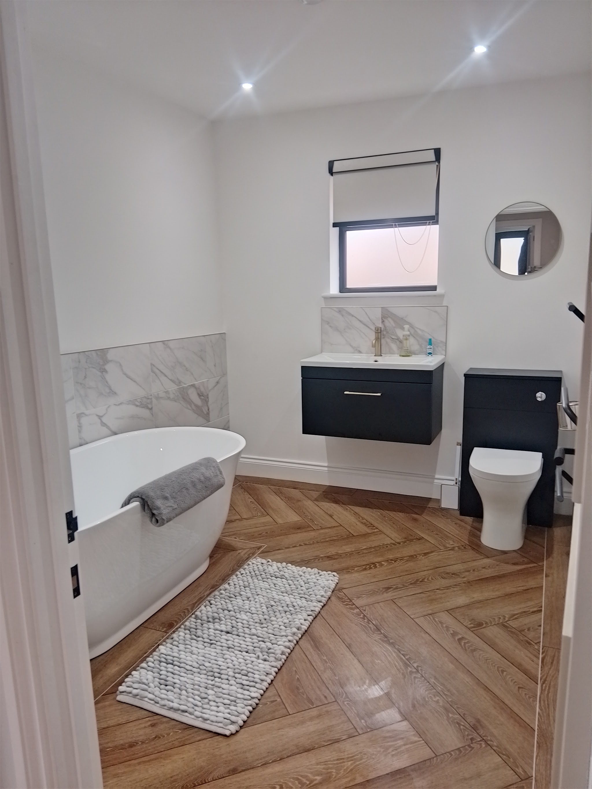Finished bathroom with a freestanding bath, white walls and a dark vanity unit